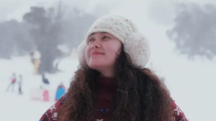 A woman in a fur-lined hat smiling up at the falling snow, graded with the Minimal look